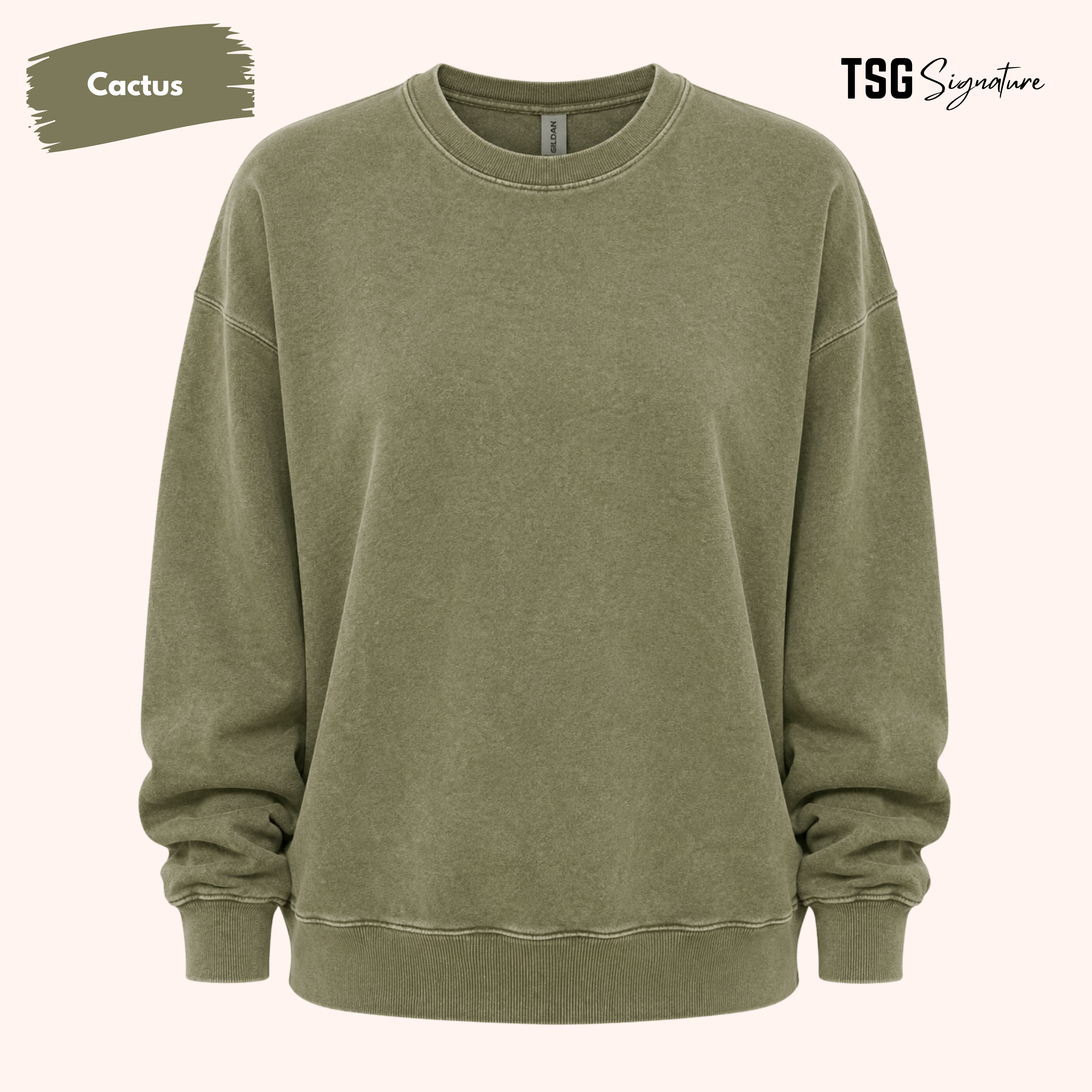 An oversized crewneck sweatshirt in a washed, muted olive green color, labeled 'Cactus' in the top left corner with 'TSG Signature' in the top right, set against a solid pale pink background.