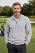 A man wearing a light gray heathered quarter-zip pullover sweater over a white collared shirt, standing on a golf course with a golf bag in the background.