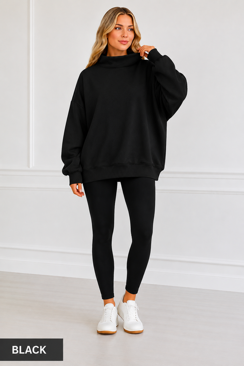 A woman modeling an oversized black sweatshirt with a mock neck, paired with black leggings and white sneakers, standing against a white paneled wall. A black label in the bottom left corner reads 'BLACK'.