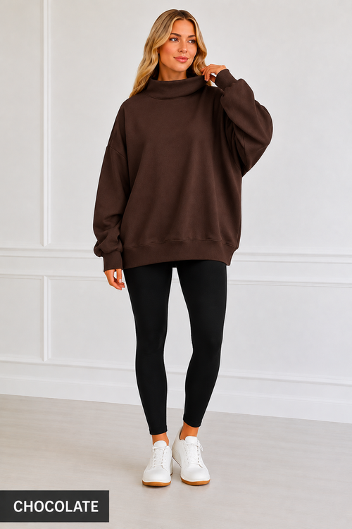 A woman modeling an oversized dark brown mock-neck sweatshirt with black leggings and white sneakers, standing against a white paneled wall. A black label in the bottom-left corner reads 'CHOCOLATE'.
