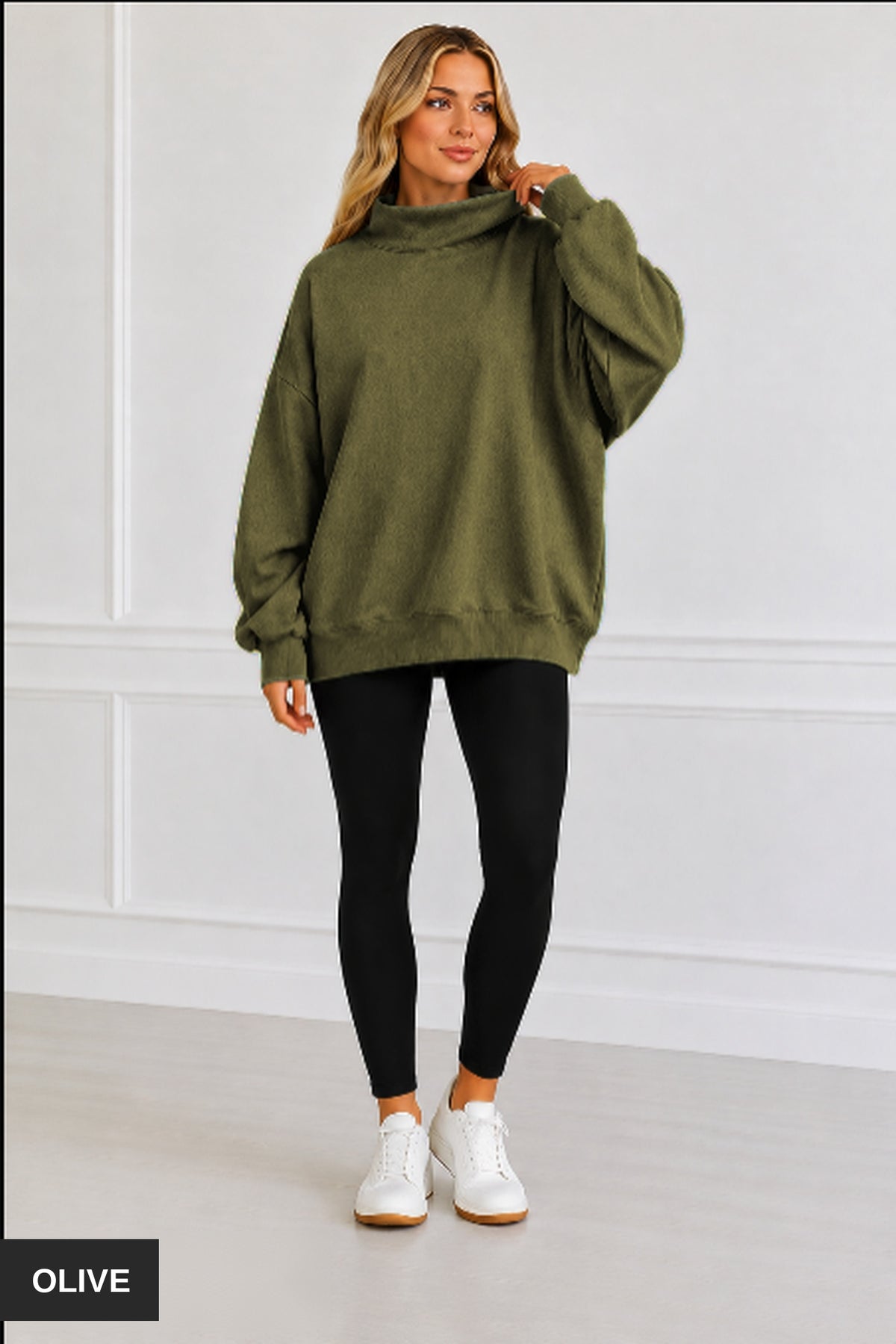 A woman modeling an oversized olive green mock-neck sweatshirt, paired with black leggings and white sneakers, standing against a white paneled wall. An 'OLIVE' color label is visible in the bottom-left corner.